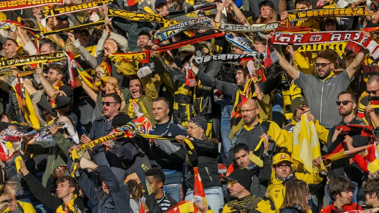 Bundesliga stadium terrace with supporters behind a yellow wall of flags