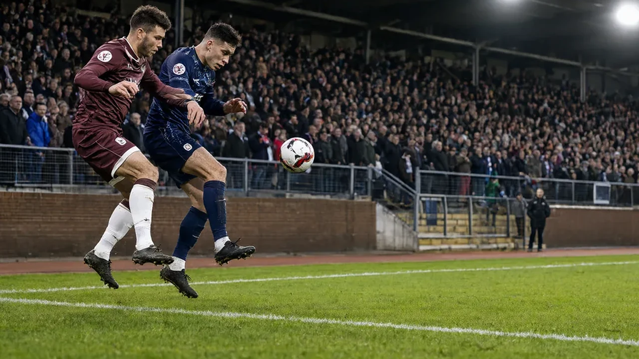 Two players in lower-league kits challenging for the ball beside a packed terrace