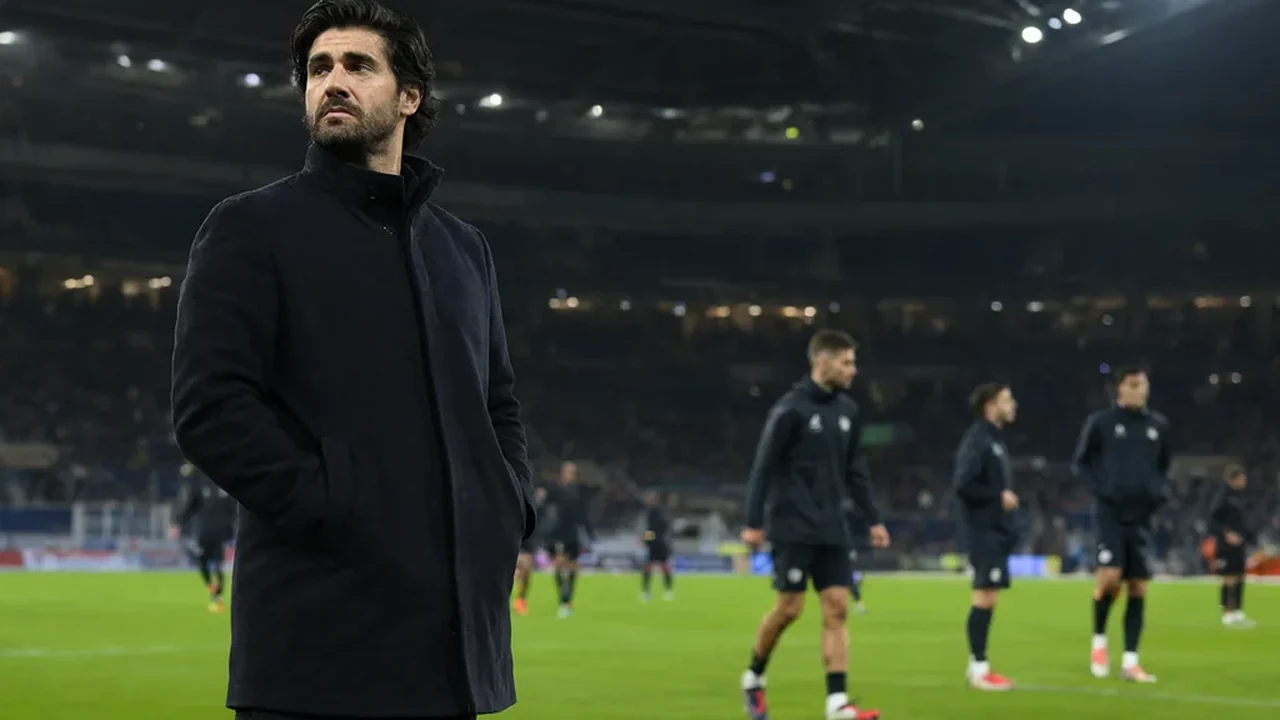 A head coach standing alone at the edge of the technical area during a night match