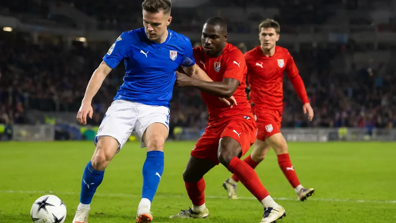A midfielder in a blue shirt driving forward on the pitch while two defenders in red challenge him at night