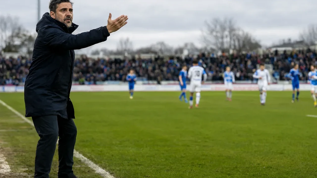 A manager in a dark coat gesturing from the edge of the technical area