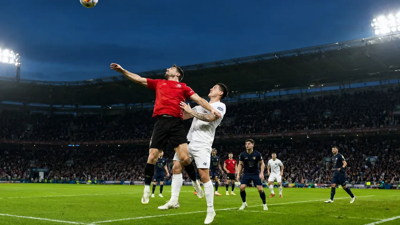 Two footballers jumping for a header in a floodlit penalty area