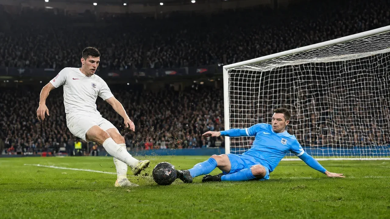 A Tottenham player in a white kit striking a shot as a goalkeeper in blue dives across the goal-line