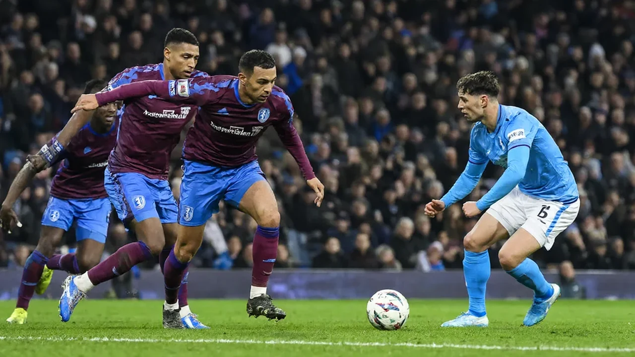 Two players contesting a bouncing ball in a crowded penalty area under floodlights